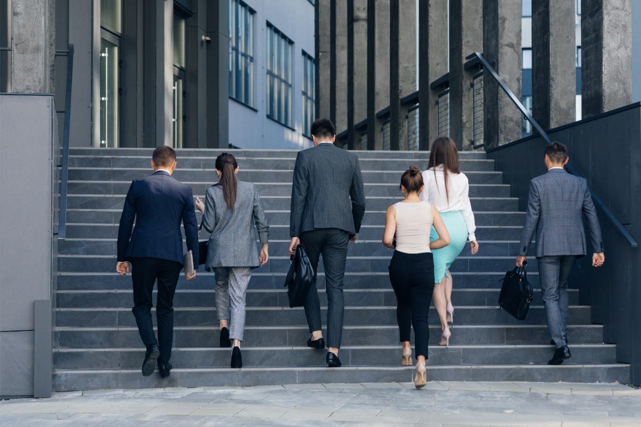 Six business people walking up the steps of their office buildings entrance as they return to work